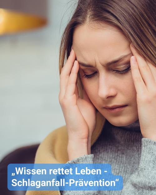 Nahaufnahme einer jungen Frau mit hellbraunem Haar, die offensichtlich Unbehagen oder Schmerzen empfindet. Sie hält sich mit beiden Händen, die Stirn gerunzelt, und ihr Gesichtsausdruck zeugt von Schmerzen oder Angst. Ihre Augen sind geschlossen.  Sie trägt einen grauen Rollkragenpullover, der über einem senfgelben Schal oder einer Decke liegt. Der Hintergrund ist verschwommen, was auf eine Innenraumszene mit gedämpften Farben hinweist.  Am unteren Rand des Bildes ist ein Textfeld eingeblendet. Der Text lautet: „Wissen rettet Leben - Schlaganfall-Prävention“.